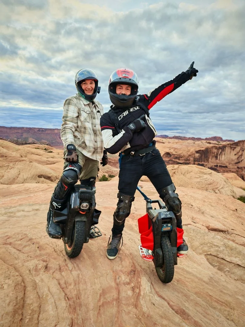 Lauren Ford and James Darnell standing on their electric unicycles on slickrock, both in helmets and protective gear