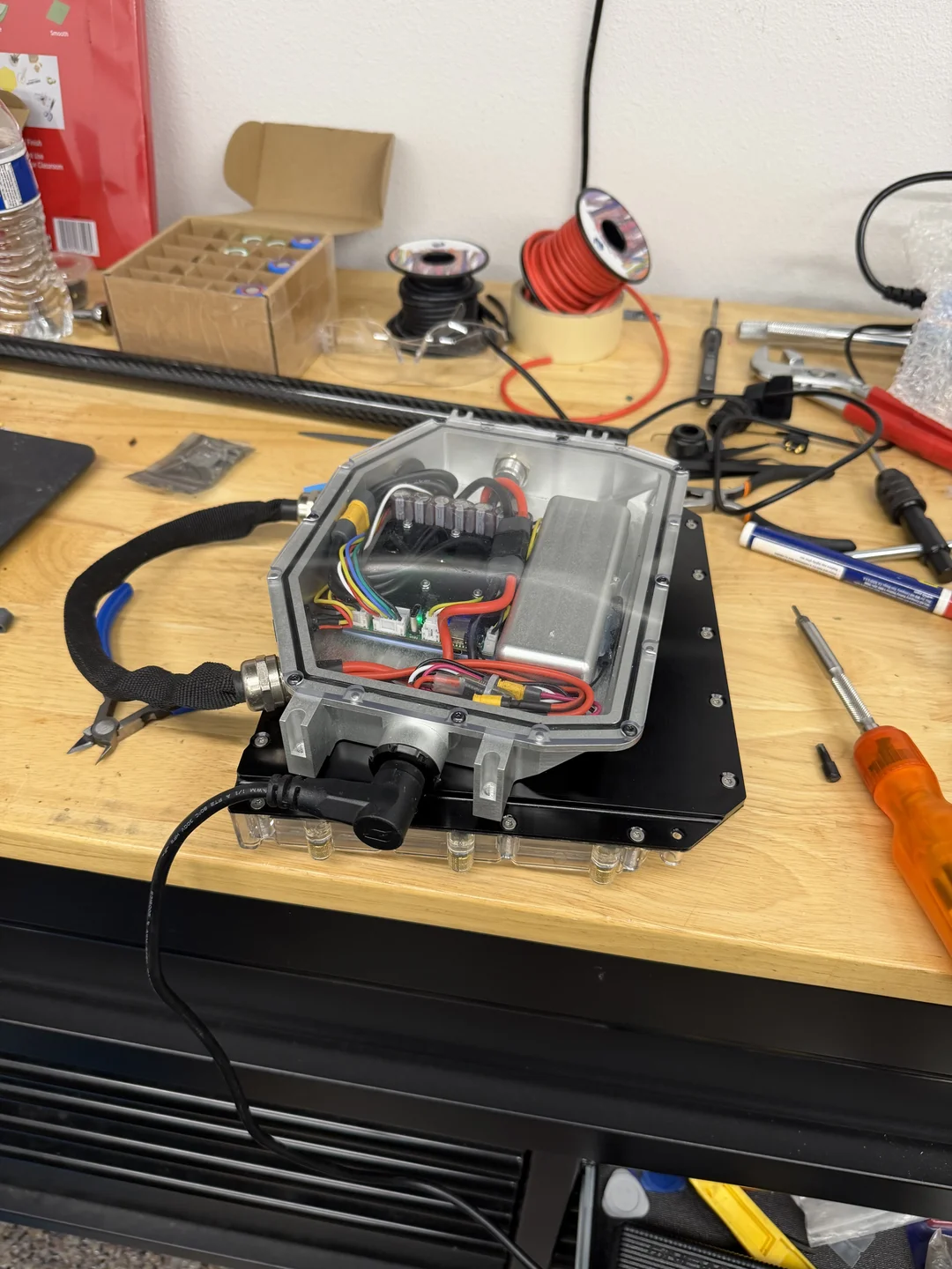 An open aluminium and clear-topped controller enclosure on a workbench, showing internal wiring, a capacitor bank and a heatsink, mounted to a black baseplate